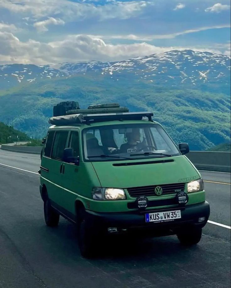 a green van driving down the road with mountains in the background