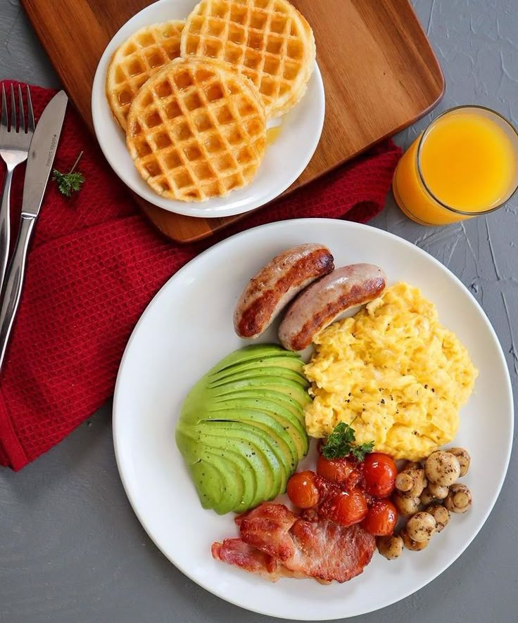 two plates with breakfast foods on them next to a glass of orange juice