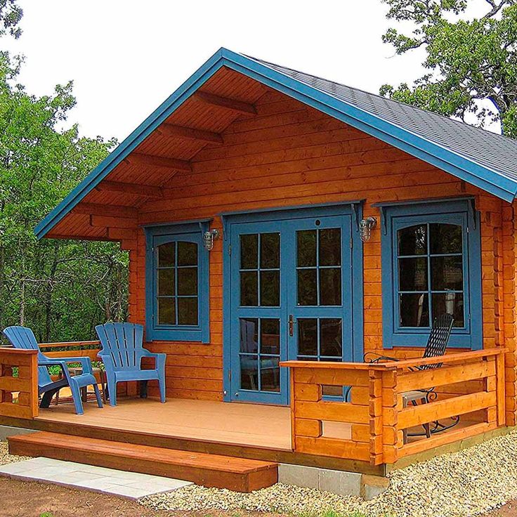 a small wooden cabin with blue doors and two chairs on the front porch next to it