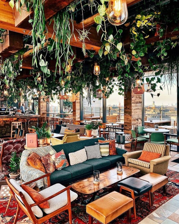 a living room filled with lots of furniture and plants hanging from the ceiling above it