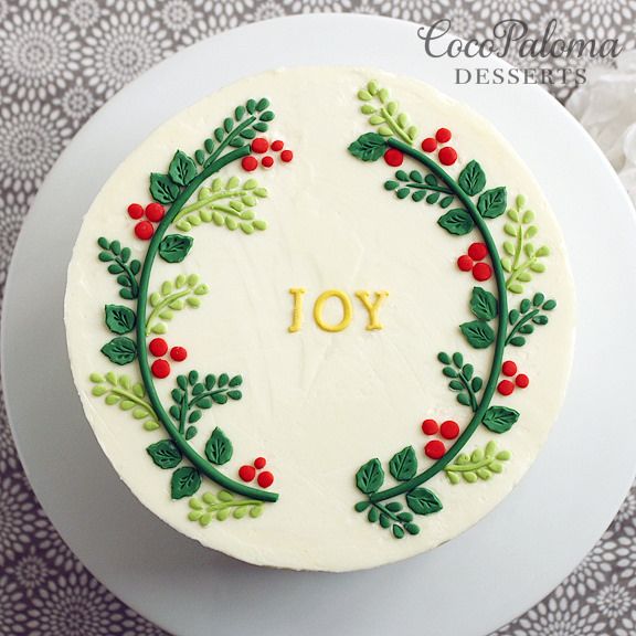 a cake decorated with holly leaves and the word joy in gold lettering on top is sitting on a white plate