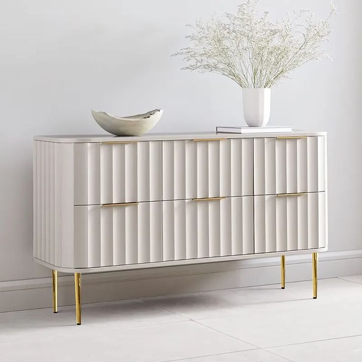 a white cabinet with two drawers and a bowl on top, in front of a wall