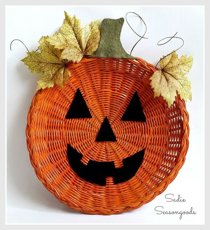 a woven pumpkin basket with leaves on the top and an evil face carved into it