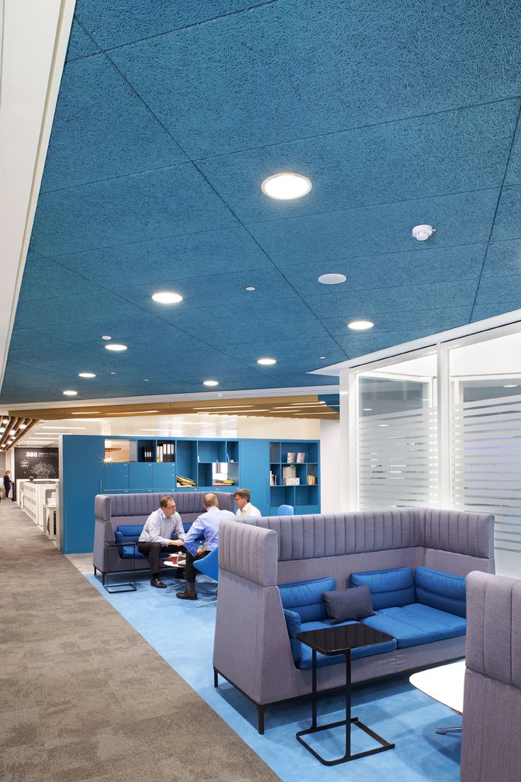 people are sitting at tables in an office setting with blue walls and ceiling lighting above them