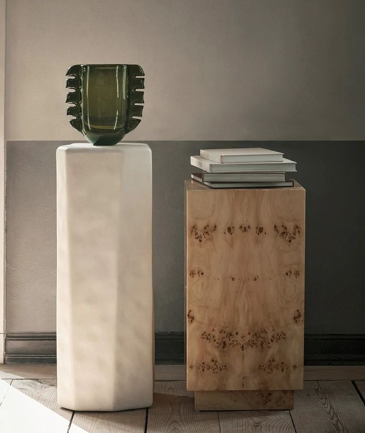 a white vase sitting on top of a wooden table next to a book case and books