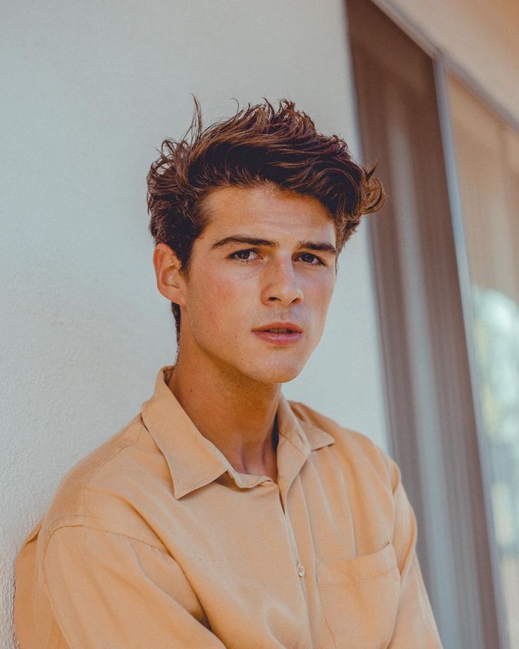 a young man leaning against a wall with his arms crossed