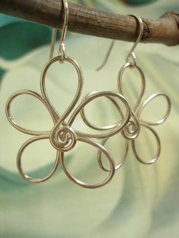 a pair of silver earrings sitting on top of a wooden stick next to a flower