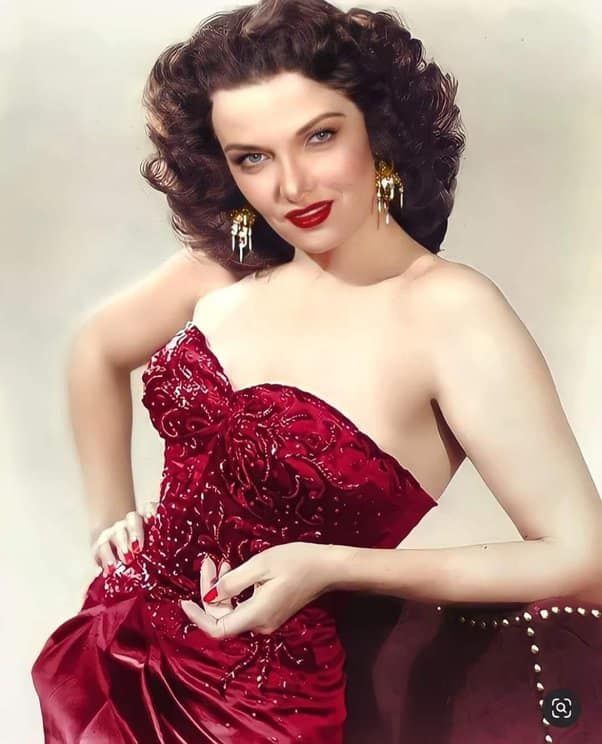 a woman in a red dress posing with her hand on her hip and wearing gold earrings