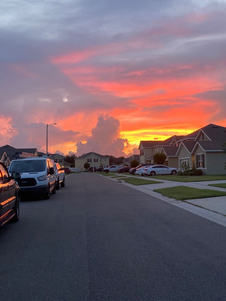 cars are parked on the street in front of houses as the sun is going down