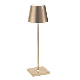 a lamp that is on top of a white surface with a metal base and a gold shade