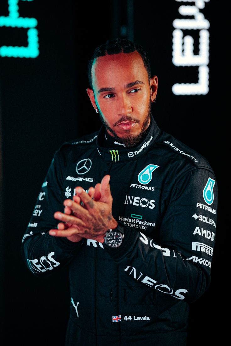 a man standing in front of a black background holding his hands together and looking at the camera