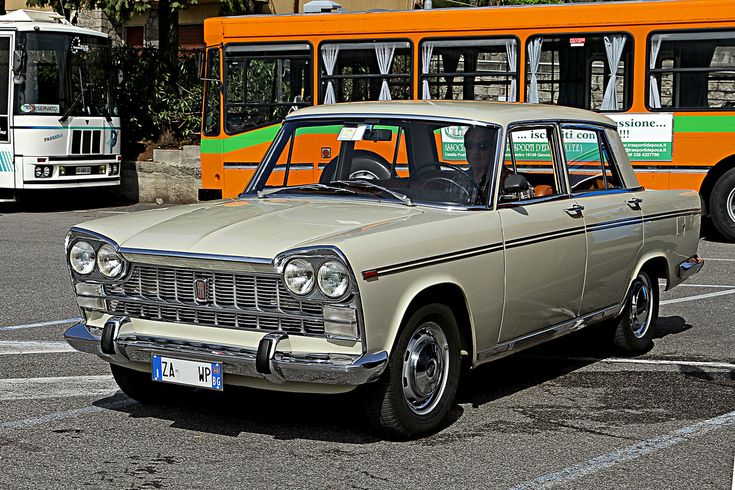 an old car is parked in the parking lot next to two other buses and one orange bus