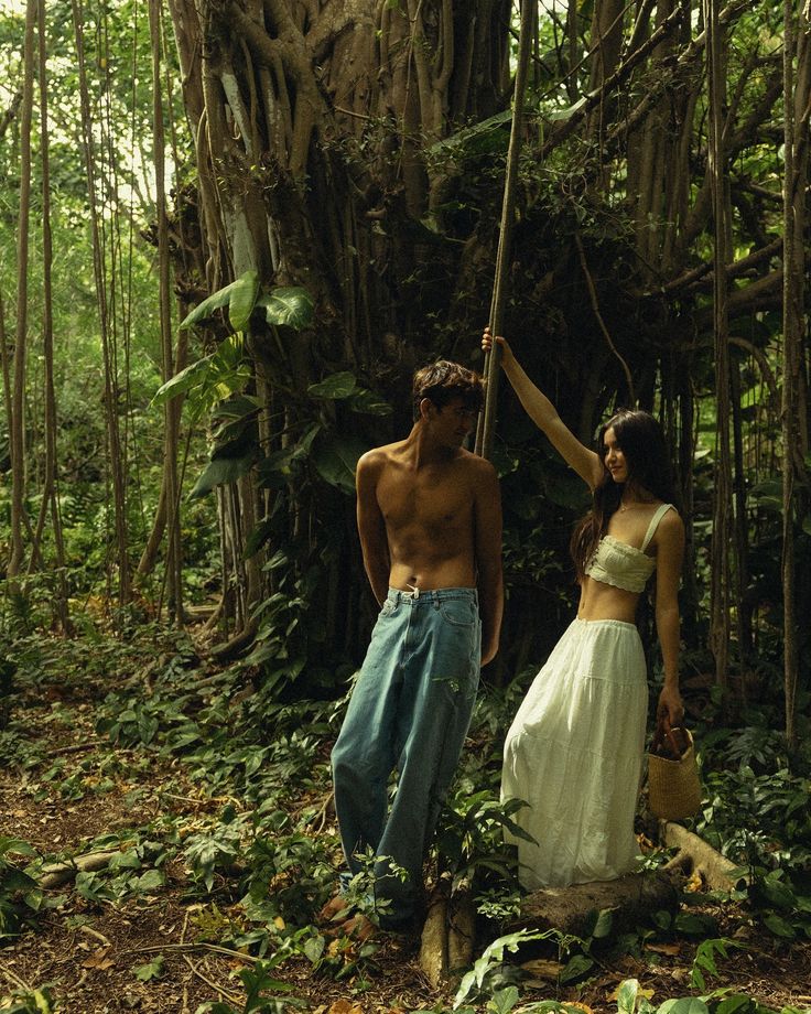 two people standing in the middle of a forest with trees and plants all around them