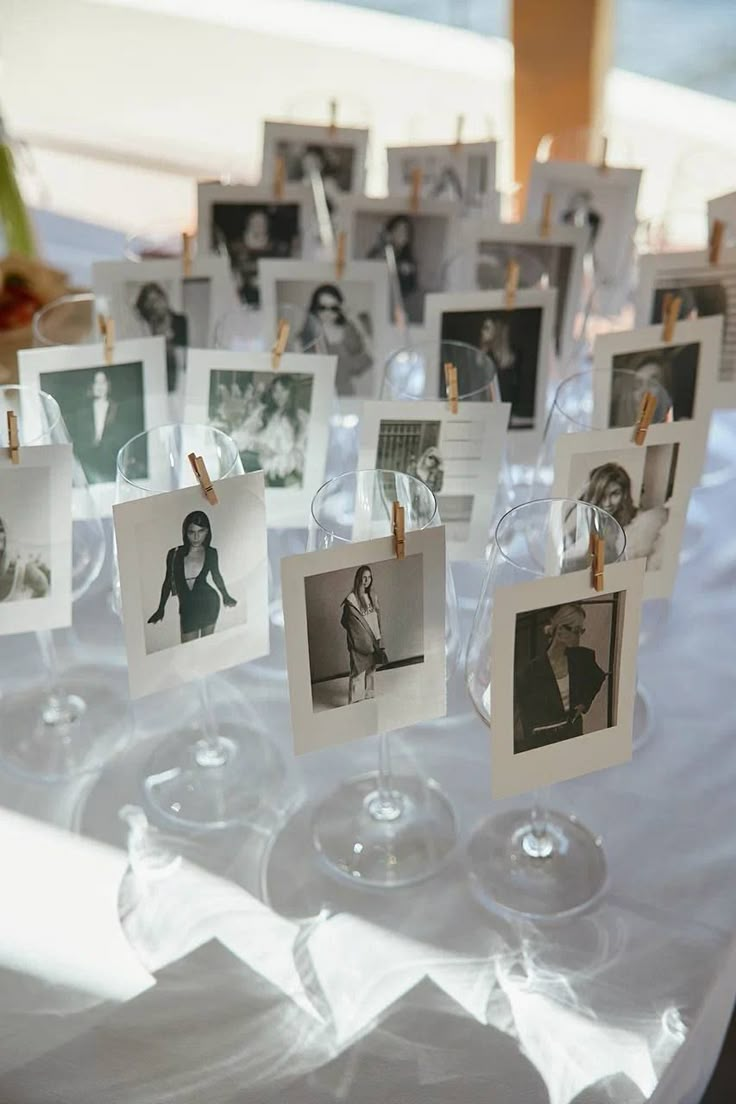 many pictures are hanging on clothes pins and glass goblets with wine glasses in the foreground