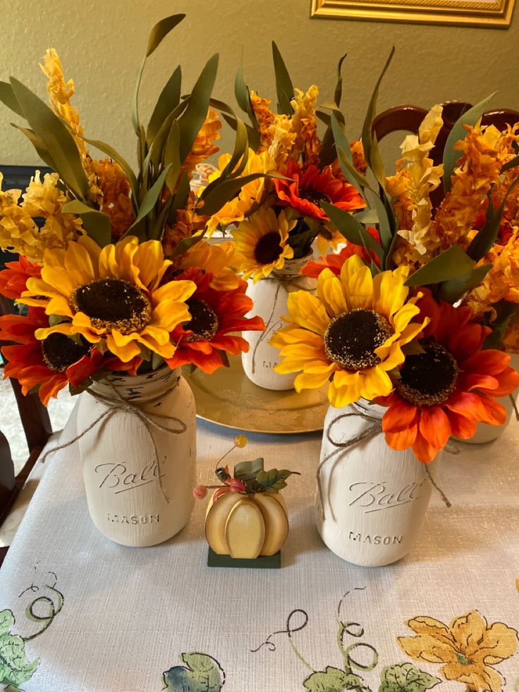 three vases with sunflowers and pumpkins on a table cloth in front of a mirror