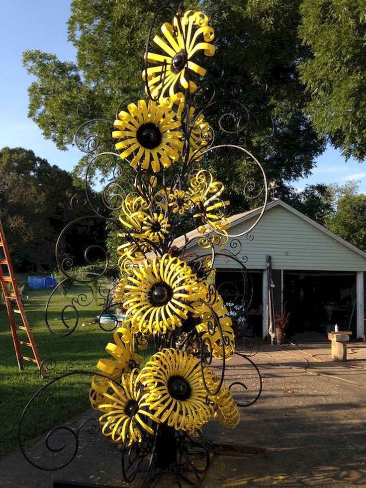 a metal sculpture with sunflowers on it in front of a house and trees