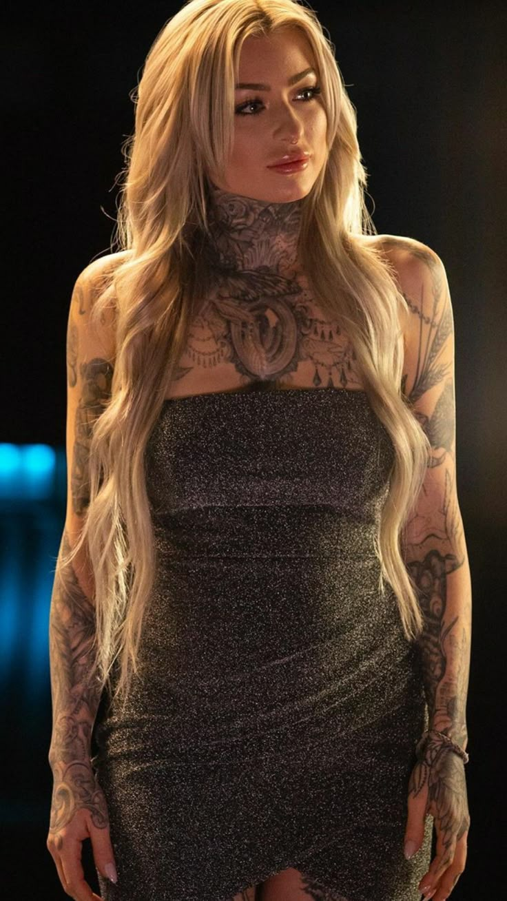 a woman with tattoos on her chest and arm is standing in a dark room wearing a dress