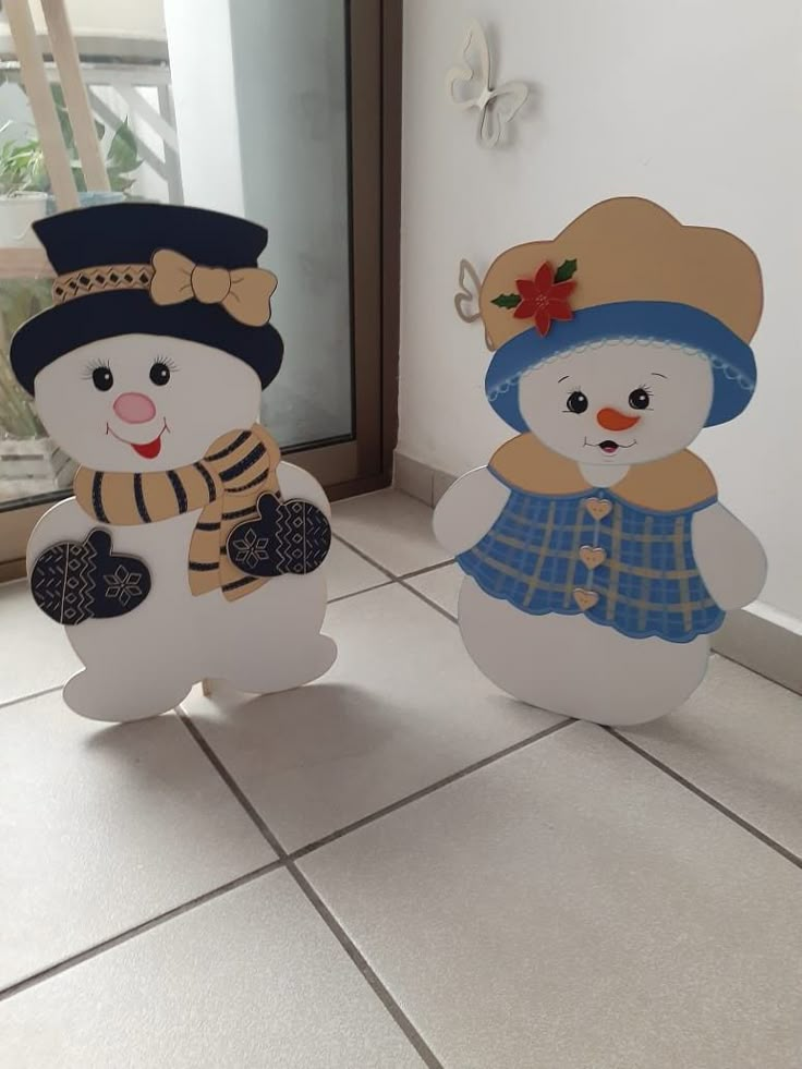 two snowmen standing next to each other on a tile floor in front of a window