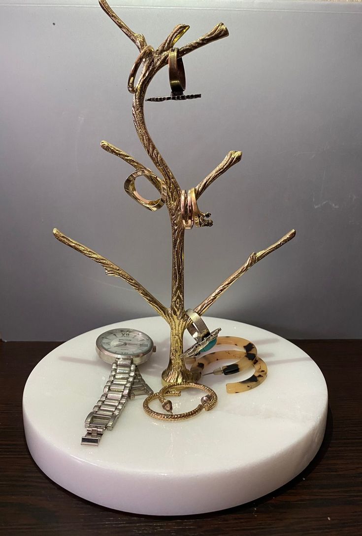 there is a gold tree on top of a white stand with bracelets and watch