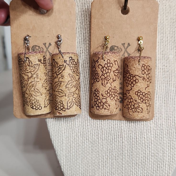 three cork earrings with designs on them being held by a person's hand,