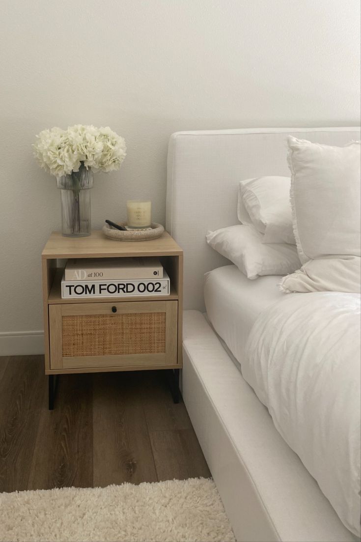 a bed with white sheets and pillows next to a night stand on a wooden floor