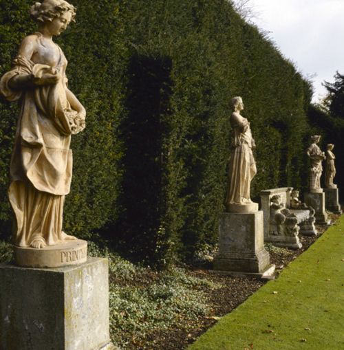 some statues are standing in the grass next to bushes and hedges with green plants on either side