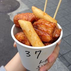 a person holding a cup filled with fried food on top of a street side walk