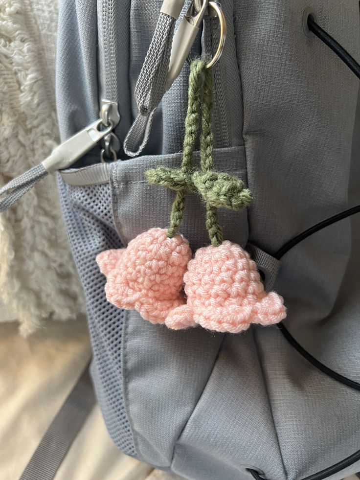 two crocheted pink flowers are hanging from a hook on the back of a backpack