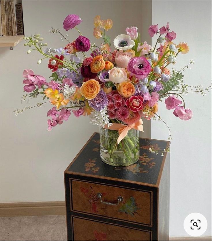 a vase filled with lots of colorful flowers on top of a wooden dresser next to a wall