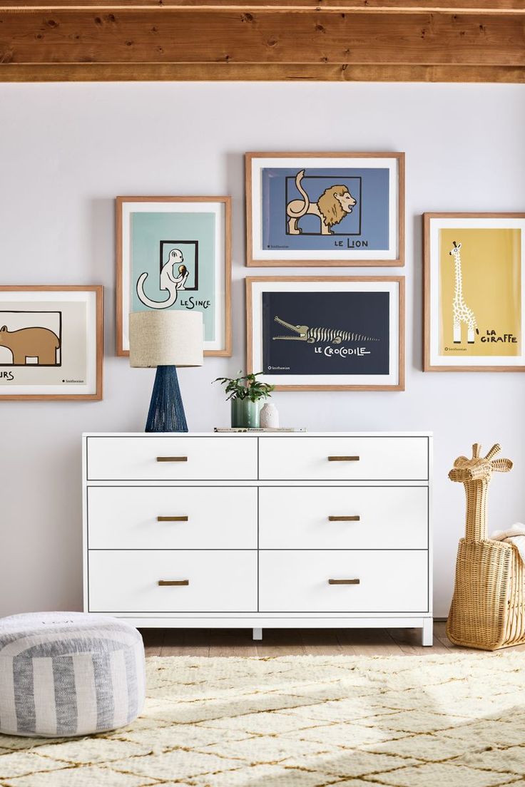 a white dresser sitting next to a wall with pictures on it