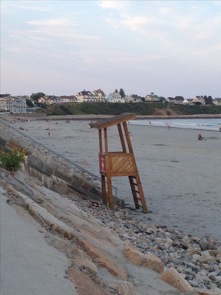 a wooden chair sitting on top of a sandy beach next to the ocean with buildings in the background