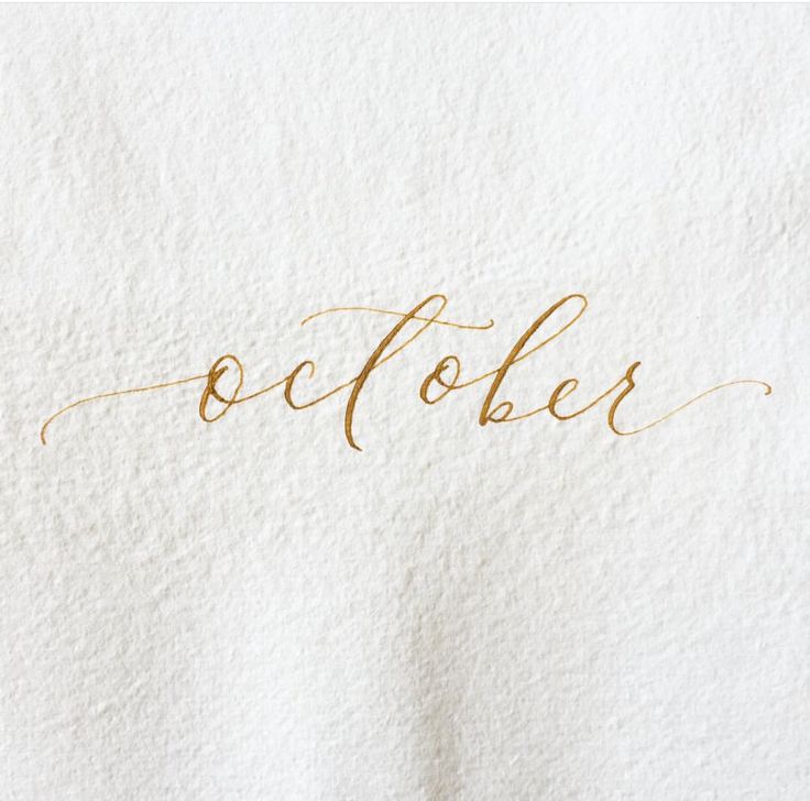 the word october written in cursive gold ink on a white sheet of paper