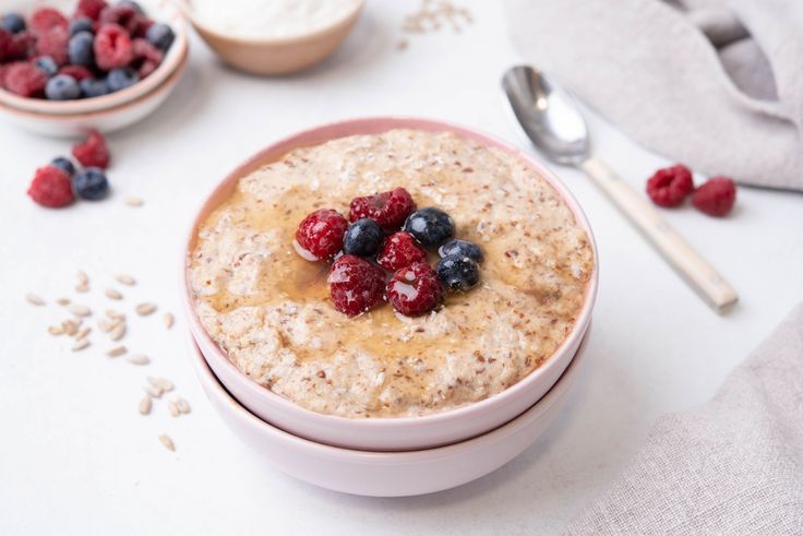 a bowl of oatmeal with berries and blueberries in it next to spoons