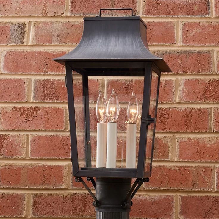 three candles are lit in an old fashioned lantern on a street light pole against a brick wall