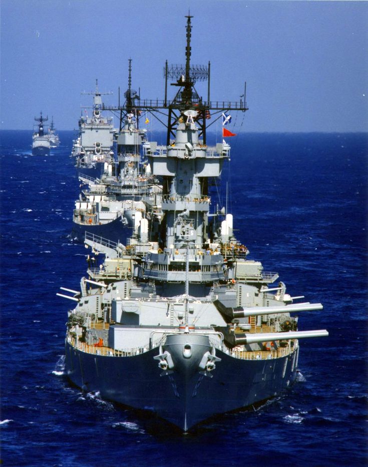 two navy ships in the middle of the ocean with one larger ship on the far side