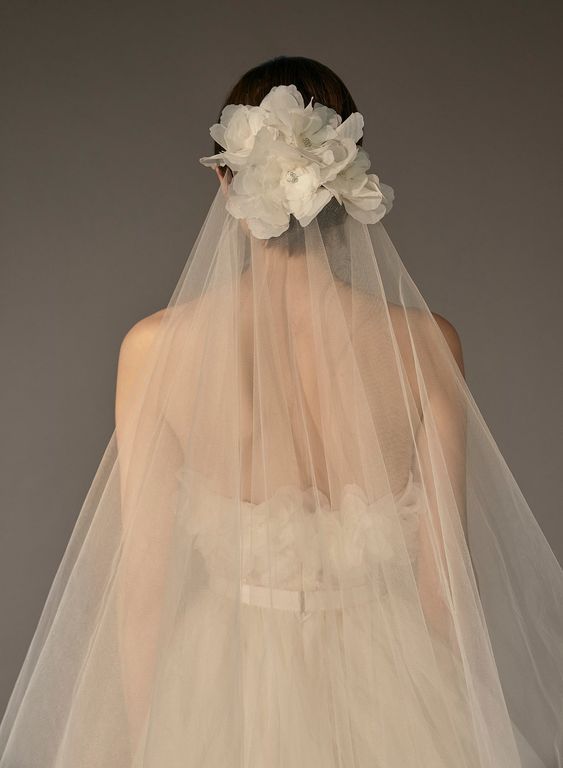 a woman wearing a wedding veil with flowers on the back of her head and neck