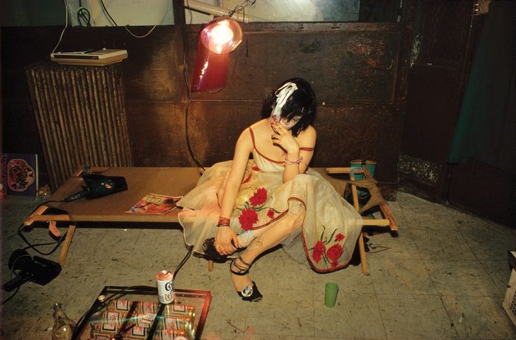 a woman sitting on top of a wooden bench in front of a table filled with items