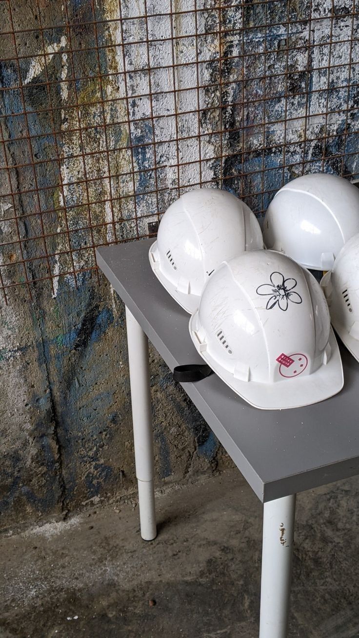 white hard hats sitting on top of a table in front of a grungy wall