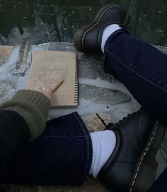 a person sitting down writing on a piece of paper with a pencil in their hand