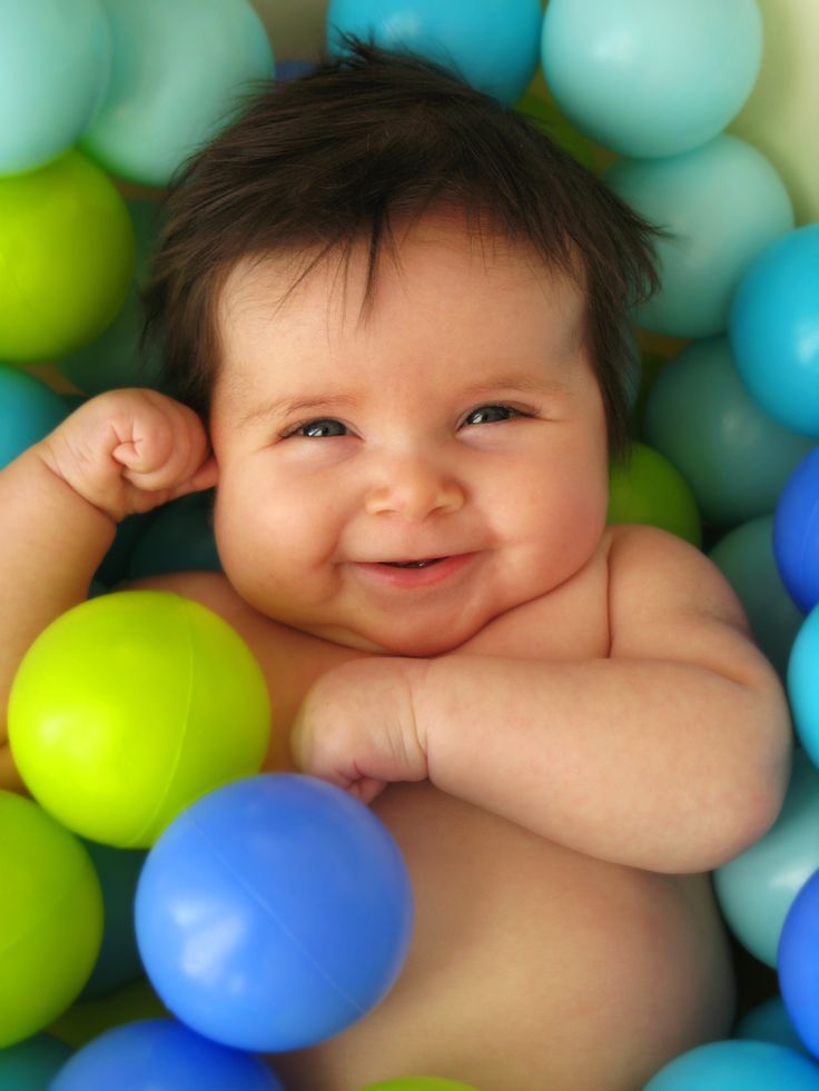 a baby in a ball pit surrounded by blue, green and yellow balls with his hands on his head