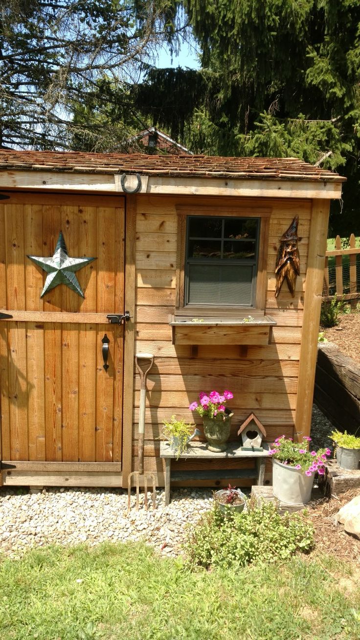 a small wooden shed with a star on the door and flowers in pots next to it