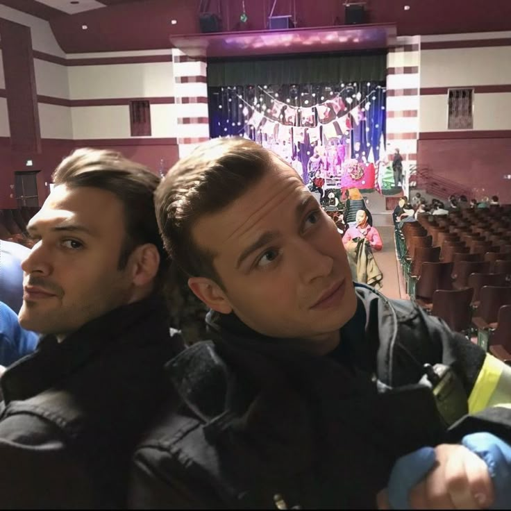 two men sitting next to each other in front of an auditorium filled with people and lights