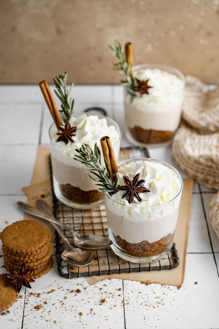 three desserts with cinnamon sticks and whipped cream in them on a cooling rack next to cookies