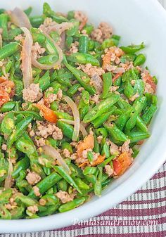 a white bowl filled with green beans, meat and veggies on top of a checkered table cloth