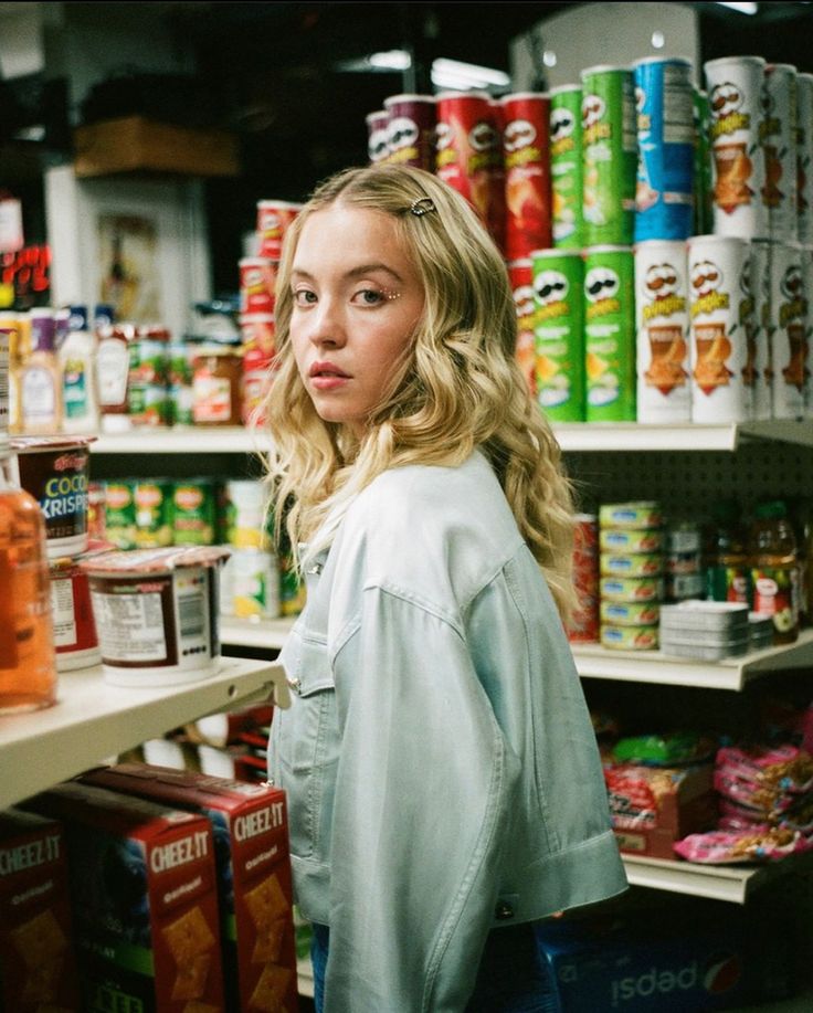 a woman standing in front of a shelf filled with canned food and other foodstuffs