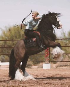 a woman riding on the back of a brown horse while holding a bow and arrow