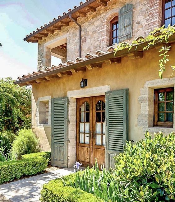 a house with green shutters on the front and side windows, surrounded by greenery