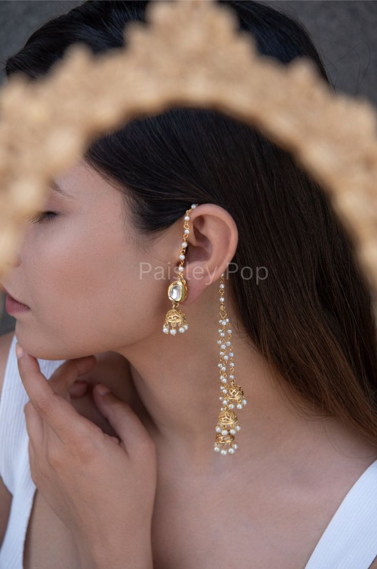 The gold-plated kundan jhumkis are traditionally inspired by the rich Indian Heritage of jewelry making. The design of the bridal jhumkis earrings features pearl hangings and a top encrusted with kundan. These ethnic jhumkis have a gold-plated pearl chain that gives them a delicate and elegant look. The richly traditional design is versatile and can be paired with almost anything Indian.  Closure - Push Back Handcrafted in Jammu and Kashmir  Paisley Pop travels the depths of India to learn techn Gold Jewellery Bridal Indian, Karnphool Earrings, Earrings With Chain Indian, Earrings On Saree, Indian Jewellery Shoot, Traditional Earrings Indian Jewelry, Indian Pearl Earrings, Ethnic Jewelry Indian, Indian Bridal Earrings