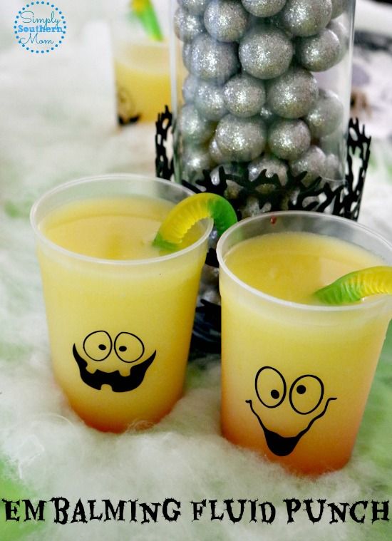 two glasses filled with liquid sitting on top of a table next to silver balls and candy