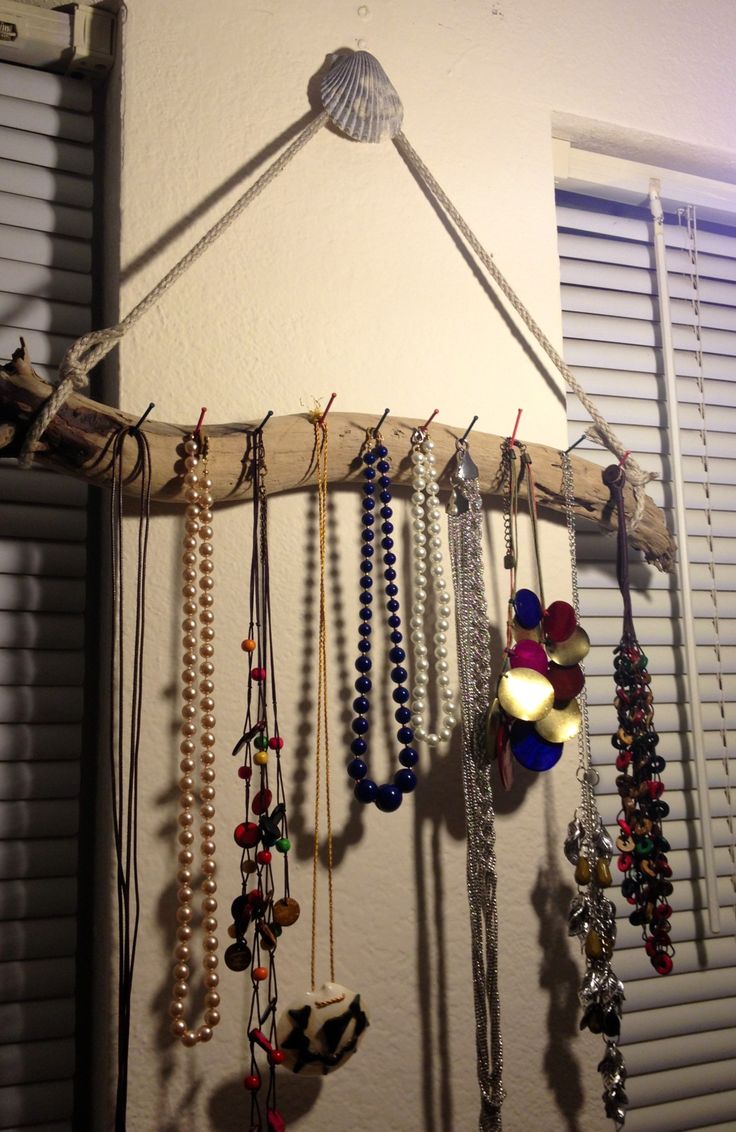 several necklaces are hanging on a wooden rack in front of a window with shutters